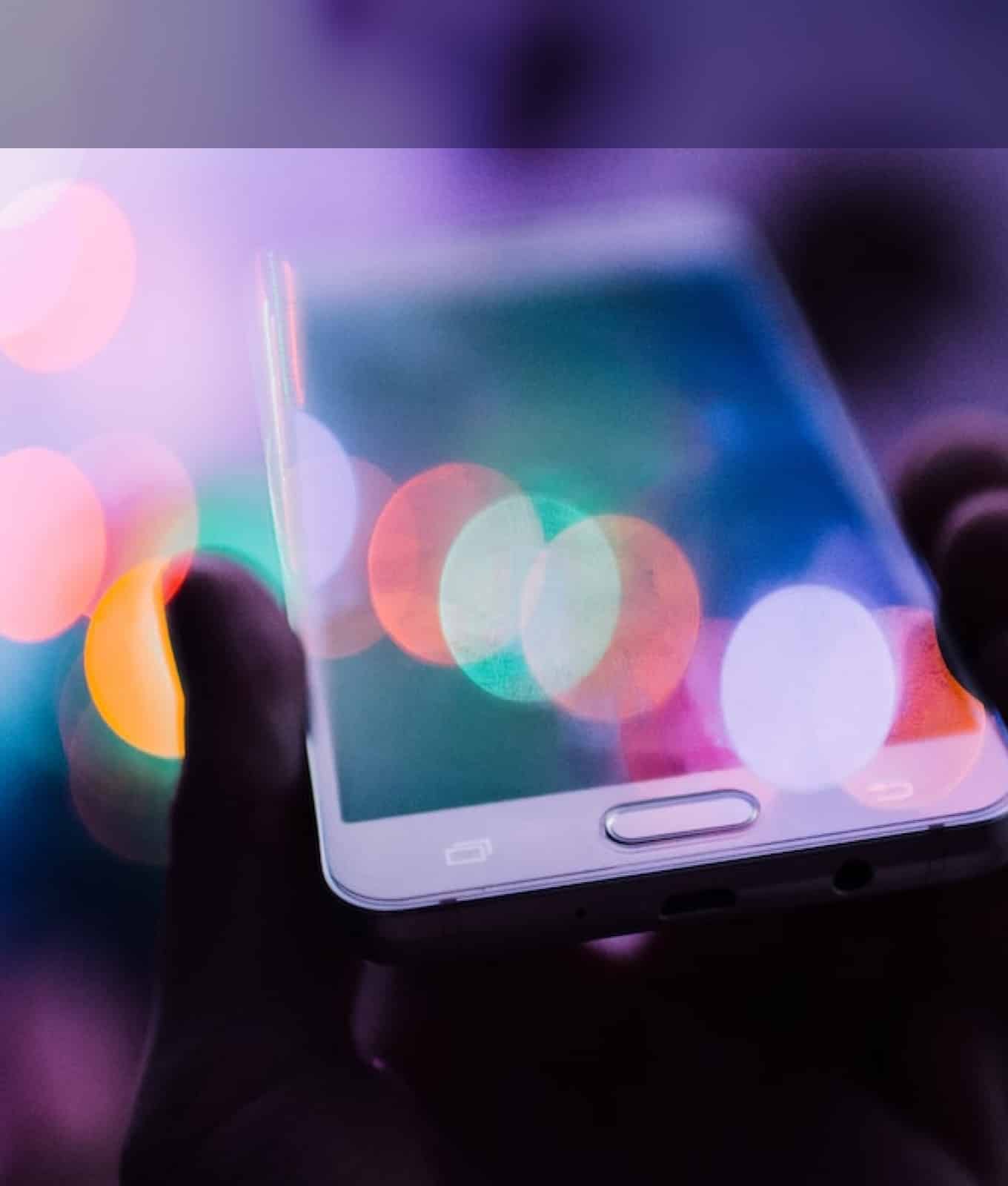 A hand holds a smartphone with a blurred, colorful bokeh effect in the background, highlighting the vibrant world of social media services.